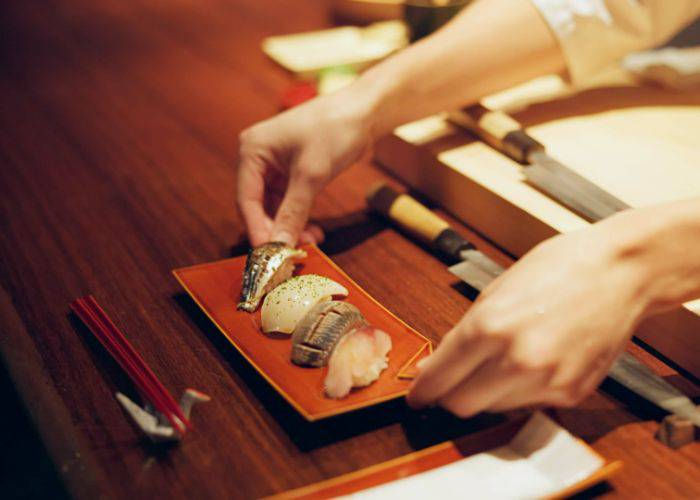 A serving tray of four nigiri sushi being served by a chef.