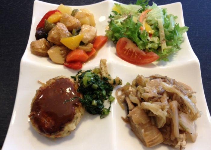 A plate with 4 partitions, each with a different Japanese vegan food such as hamburg