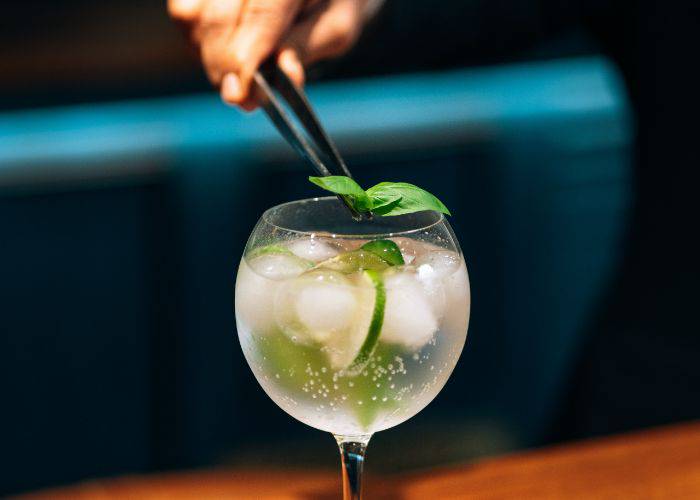 Fresh basil being added to a refreshing gin and tonic.