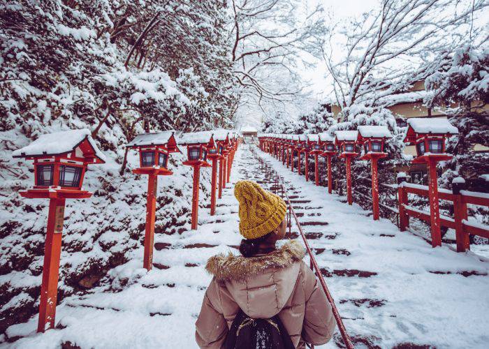 A woman wearing a coat and wooly hat while walking through the snow in Kyoto.