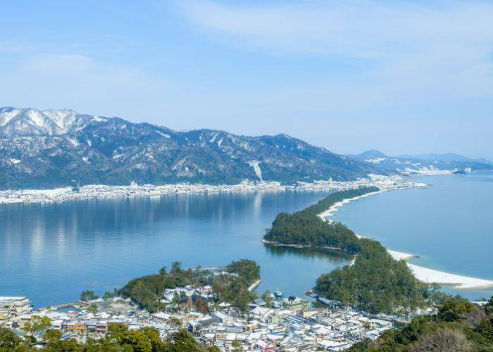 Amanohashidate as seen from a height; the mountain range in the distance is covered in snow.