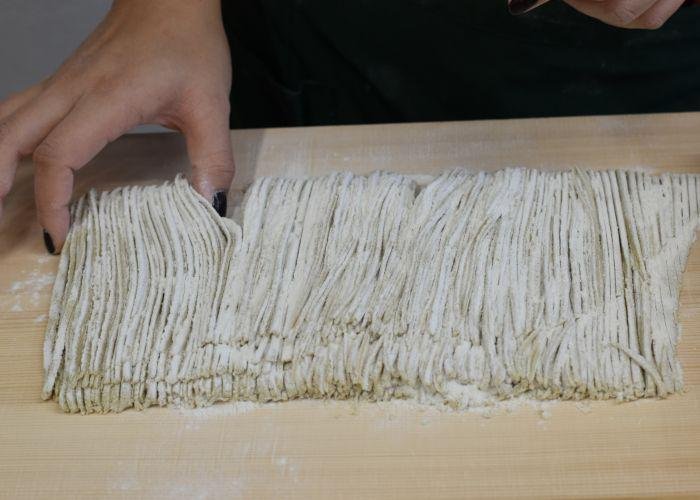Fresh cut soba noodles coated in flour, a hand picking up the noodles