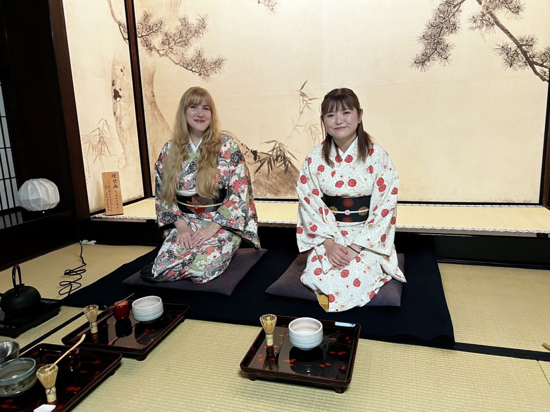 Two guests in kimono, sitting in a traditional seiza style in a Japanese teahouse.