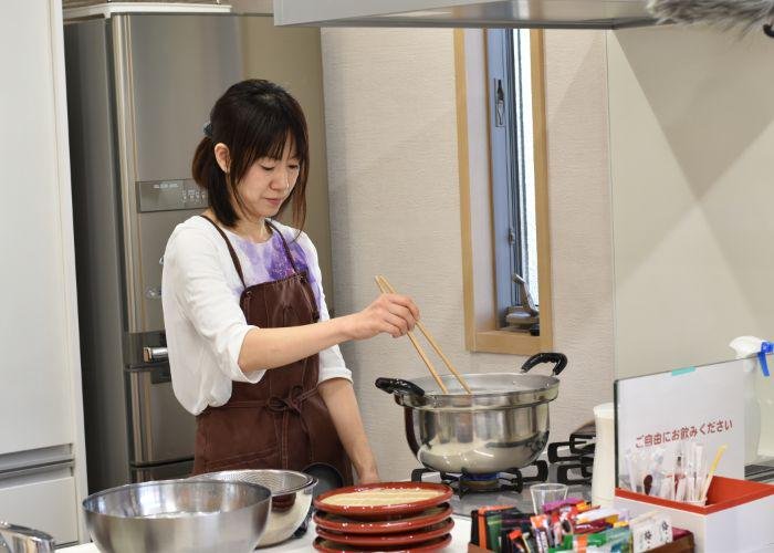 Japanese cooking instructor stands in front of the stove, stirring a boiling pot of homemade soba noodles