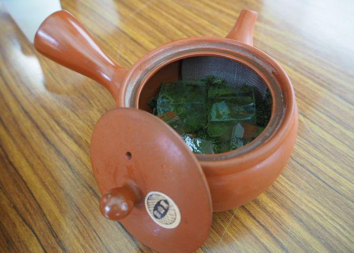 A clay tea pot with the top off so you can see inside and you can see a number of ice cubes and tea inside