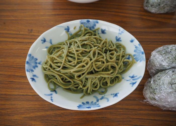 A patterned plate with green tea soba noodles and tea onigiri