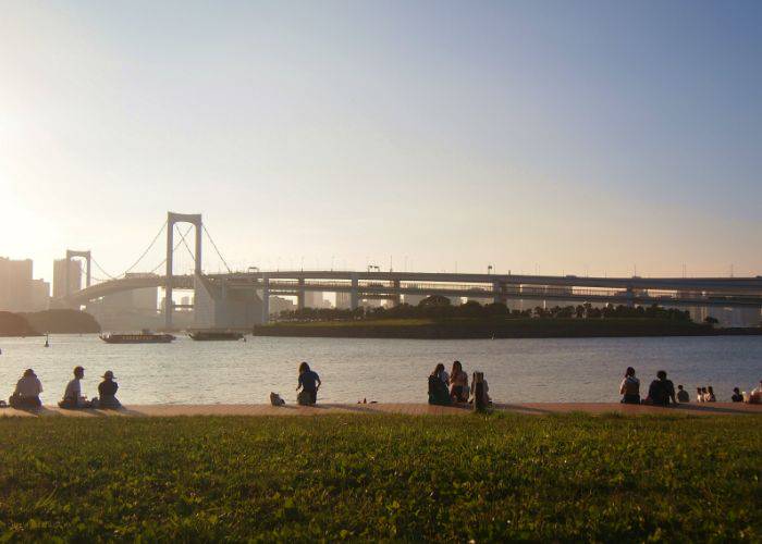 People sitting by the water and enjoying the sunset at Odaiba Marine Park.