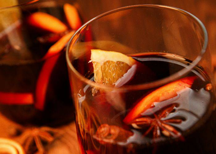 Two cups of gluhwein, garnished with orange, aniseed and cinnamon sticks.