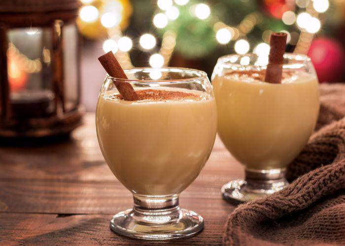 Two glasses of eggnog, topped with a dusting of cinnamon and sticks of cinnamon.