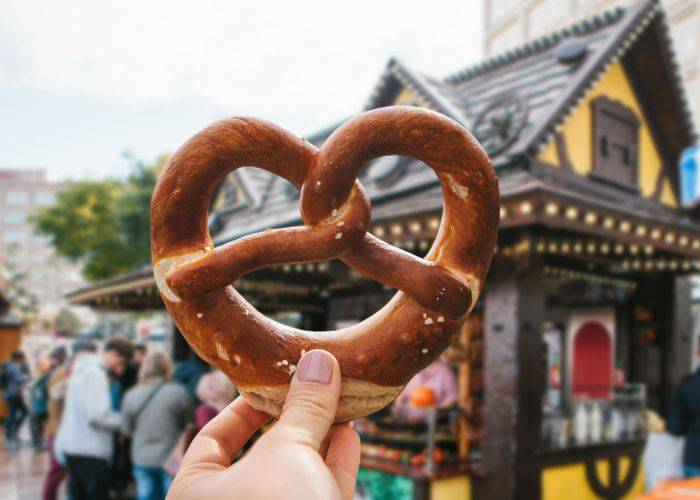 A hand holding up a fresh pretzel against a background of a Christmas market.