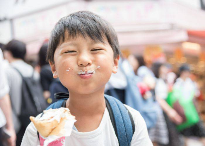 A young boy enjoyed a crepe; he has a moustache of cream.