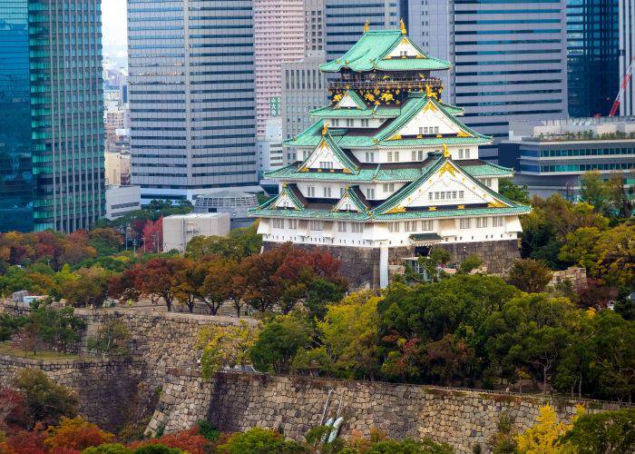 Osaka Castle set against Osaka's modern skyscrapers. Around it, fall foliage begins to show.