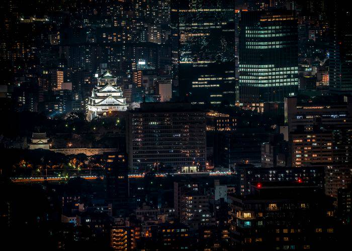 A view of Osaka Castle at night, illuminating the skyline of Osaka from afar.