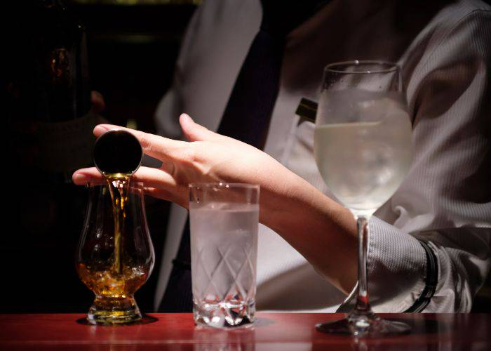 A dram of whisky being poured by a bartender.