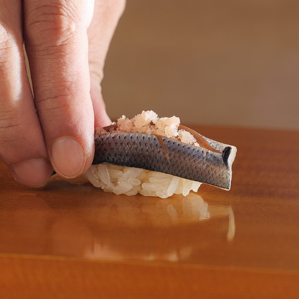 Close-up of expertly crafted sushi nigiri being placed on wooden counter