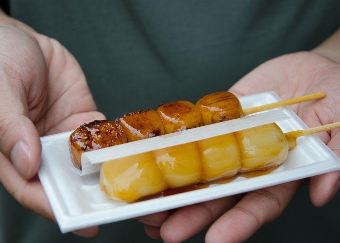 Two skewers of dango, a type of Japanese snack, with different sauces is on a white plate