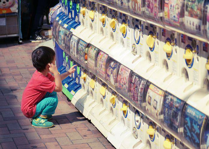 A child crouched down next to a wall of gachapon machines.