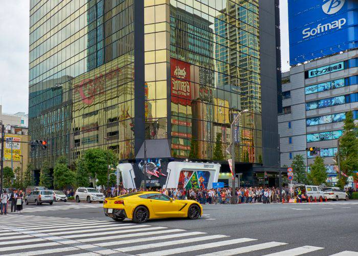 A fancy sports car driving through the center of Akihabara.