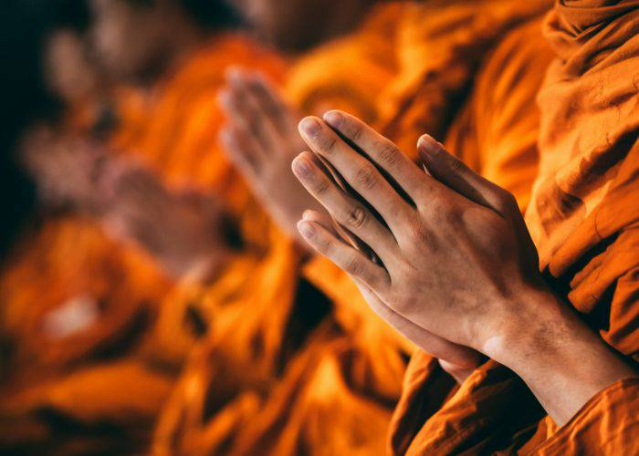 Buddhist monks in orange robes and clasped hands.