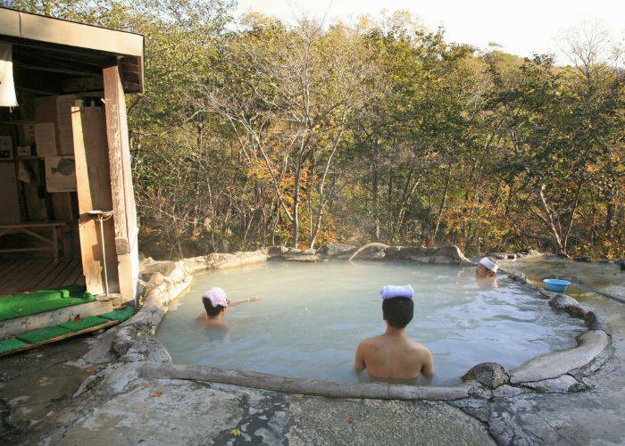 People resting in an outdoor hot spring with towels on their heads.