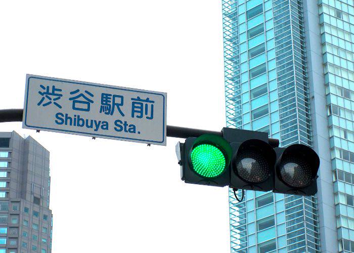 A traffic light with a sign showing the direction to Shibuya Station.