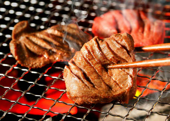 Thick slices of gyutan beef tan being grilled.