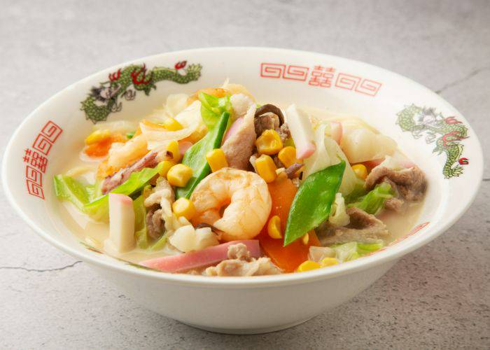 A bowl of seafood noodle soup, topped with shrimp and colorful veggies.