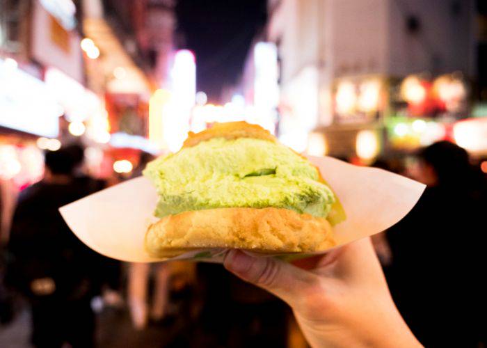 Holding melon pan with green tea ice cream inside while walking along a Japanese street at night