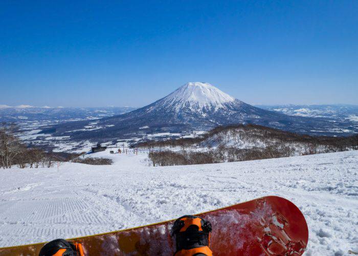 A snowboarder taking a break and resting with a view of a snow-topped mountain.