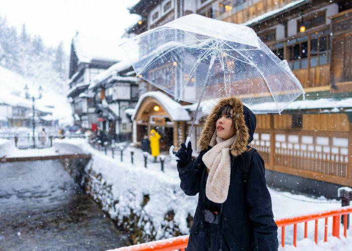 A girl in a thick coat holding an umbrella, looking up at fresh snow in Japan.