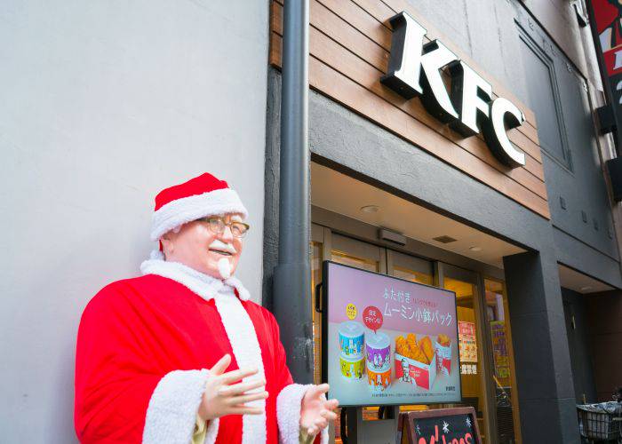 Colonel Sanders dressed up as Santa Clause outside a KFC.