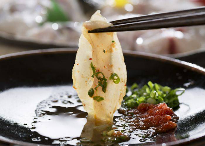 Fugu sashimi being dipped into a sauce with spring onions.