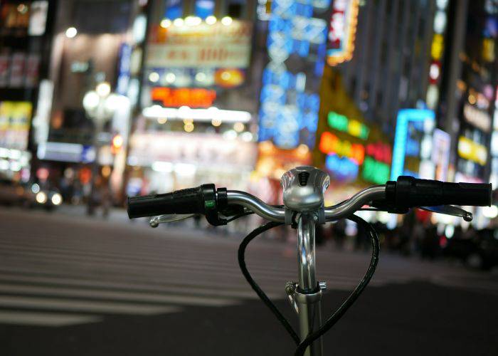 In the foreground, a bike's handlebars; in the background, Tokyo at night.