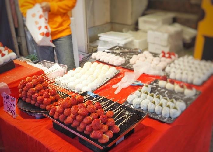 A table covered with a red cloth, with skewers of red Japanese strawberries and ichigo daifuku, strawberry mochi