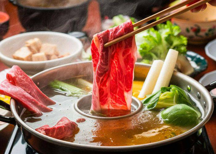 A slice of meat being dunked in a hot shabu-shabu broth.