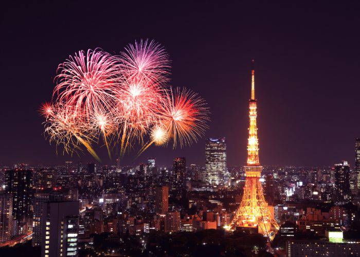 Tokyo Tower illuminated at night; beside it, fireworks explode.