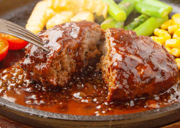 A cross section of a cooked hamburg steak with vegetables on the side