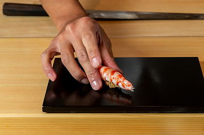 Chef placing nigiri sushi on a black plate with a knife in the background.