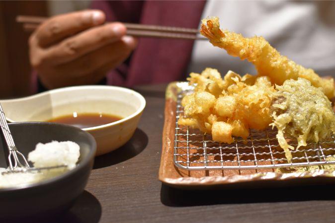 A diner about to pick up crispy tempura and dunk it in soy sauce.