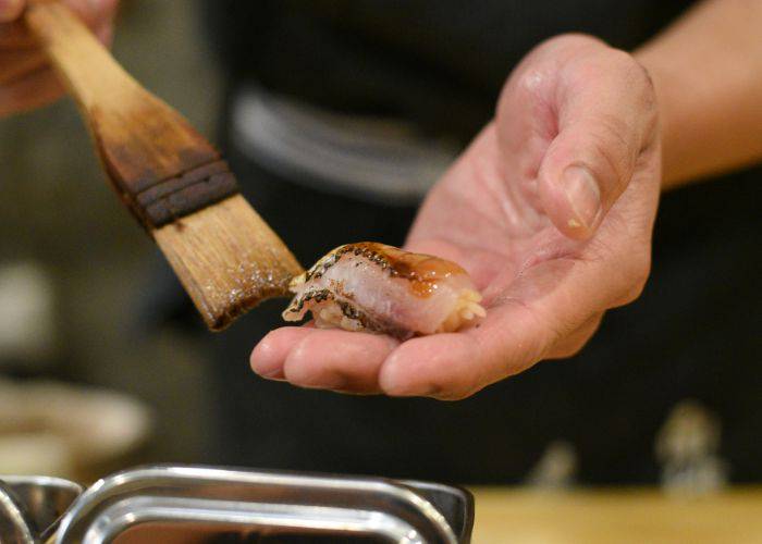 An expert sushi chef brushing premium sushi with soy sauce.