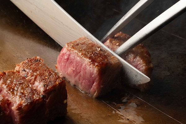 Chef slicing tender steak on a grill with precision cutting utensils