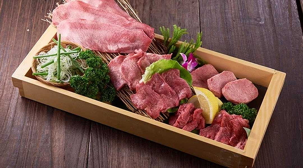 Assorted fresh meats platter with greens on wooden tray