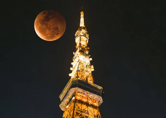 Tokyo Tower looming into the sky at night; behind it, a full moon superimposed into the image.