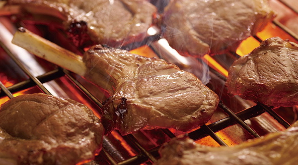 Grilled lamb chops sizzling over open flame in a restaurant setting