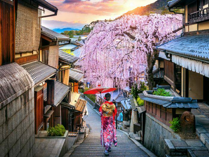 A geisha with a red paper umbrella walking through the streets of Gion.