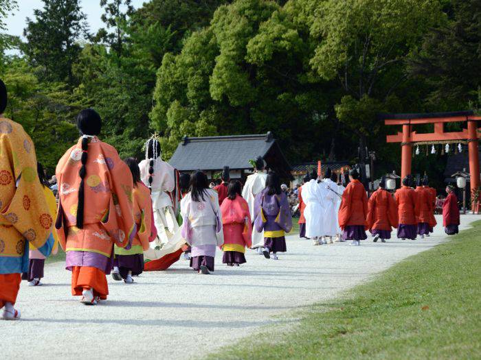 A parade walking towards a red torii gate as part of an Aoi Matsuri.