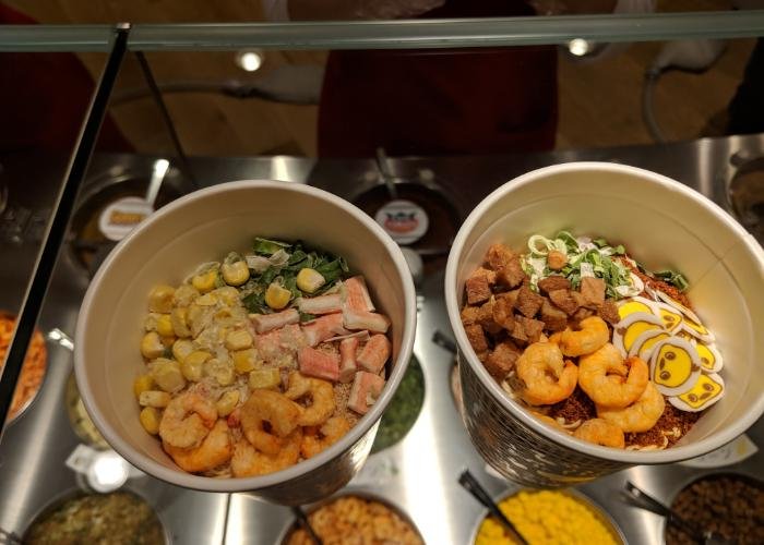 A top down view of two cup noodles, with various toppings such as corn and small shrimp