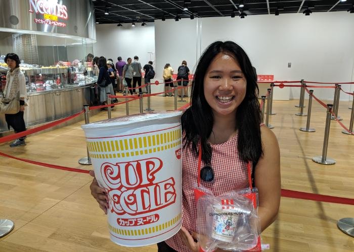 A girl with a giant Cup Noodles smiles at the Cup Noodle Museum