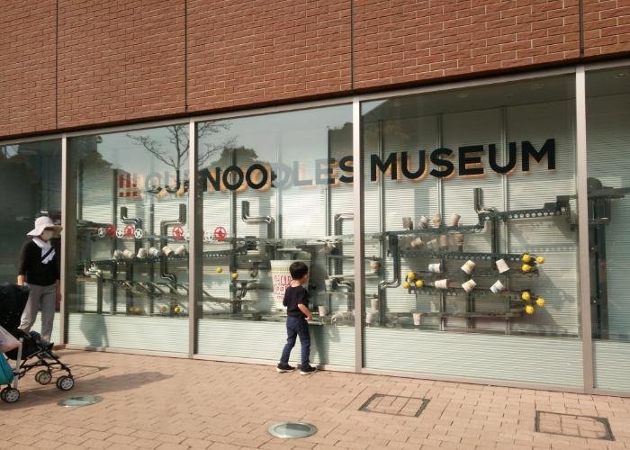Exterior of the Yokohama Cup Noodles Museum, with a small child peering into a glass window display
