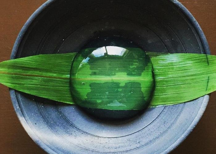 A transparent orb of Japanese raindrop cake sits on a green leaf, plated simply and elegantly
